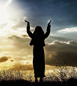 woman holding arms up in prayer and awe at sunset